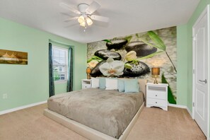 A bedroom with a bed, a ceiling fan, a nightstand, and a wall mural.