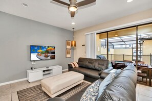 Een moderne woonkamer met een flatscreen televisie, leren banken, een witte tv-kast en een grote schuifdeur die leidt naar een buitenruimte.