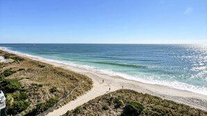 Una playa con un sendero que lleva al agua, un muelle a lo lejos y un edificio a la izquierda.