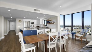 Una cocina moderna con armarios blancos, microondas y un comedor con mesa de madera y sillas blancas.
