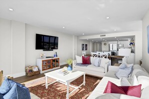 A modern living room with a white sofa, a coffee table, and a TV mounted on the wall. - Station One 8A - Upscale 3 bedroom/2 bathroom oceanfront penthouse. (Wrightsville Beach)