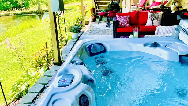 Un jacuzzi con panel de control, rodeado por un porche cubierto con un sofá y cojines rojos.