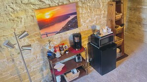 Una habitación acogedora con pared de piedra, un cuadro de un atardecer, una cafetera, un microondas y un estante de madera con diversos objetos.