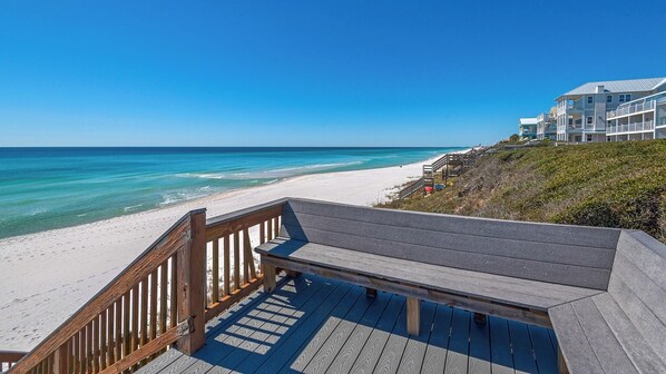 Eine Holzterrasse führt zu einem Strand mit klarem, blauem Wasser und einem weißen Sandstrand.