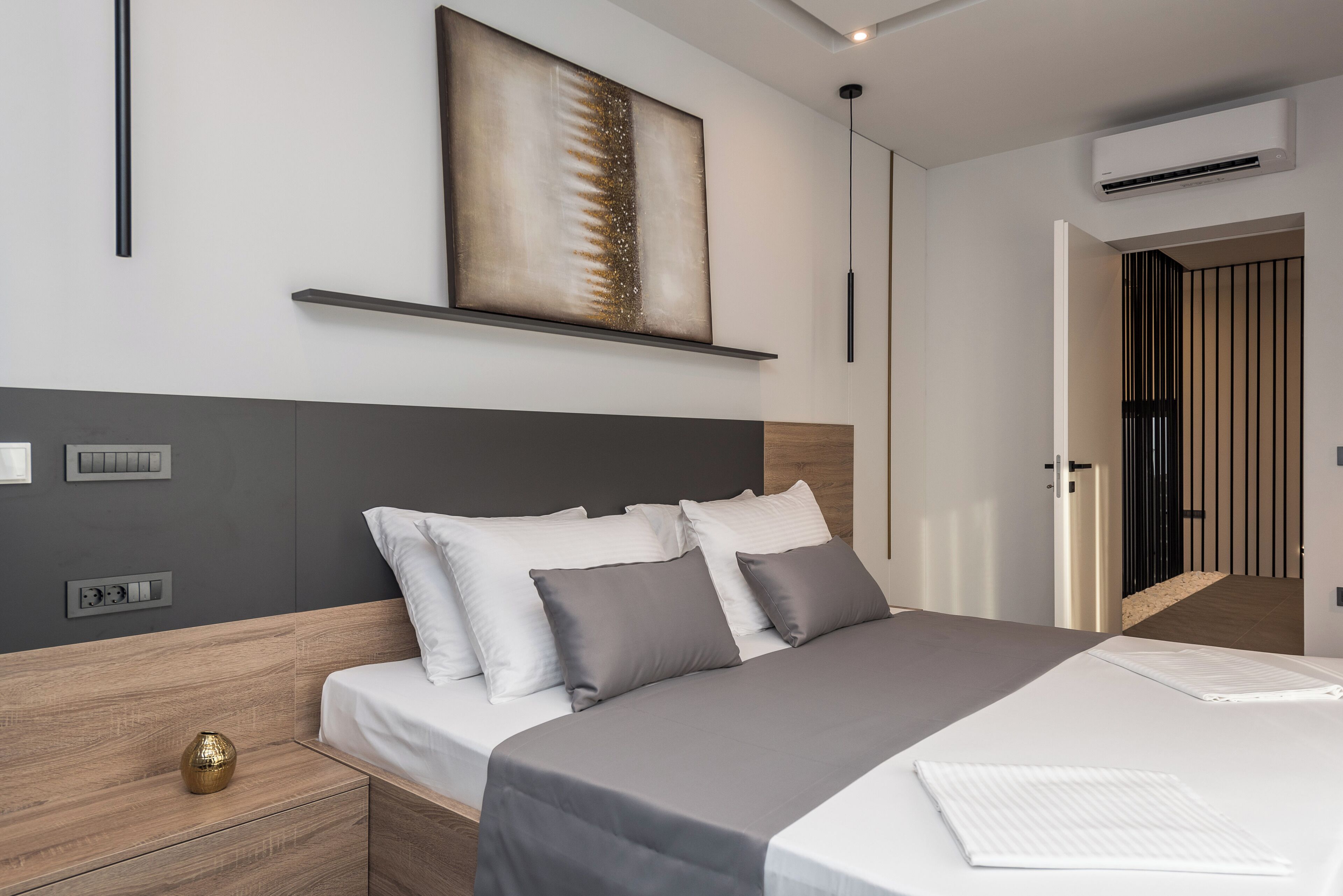 A modern bedroom with a bed, bedside tables, a wall-mounted shelf, and an air conditioning unit.