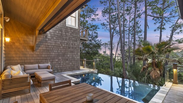 Un terrazzo in legno con piscina, area salotto all'aperto e vista sugli alberi.