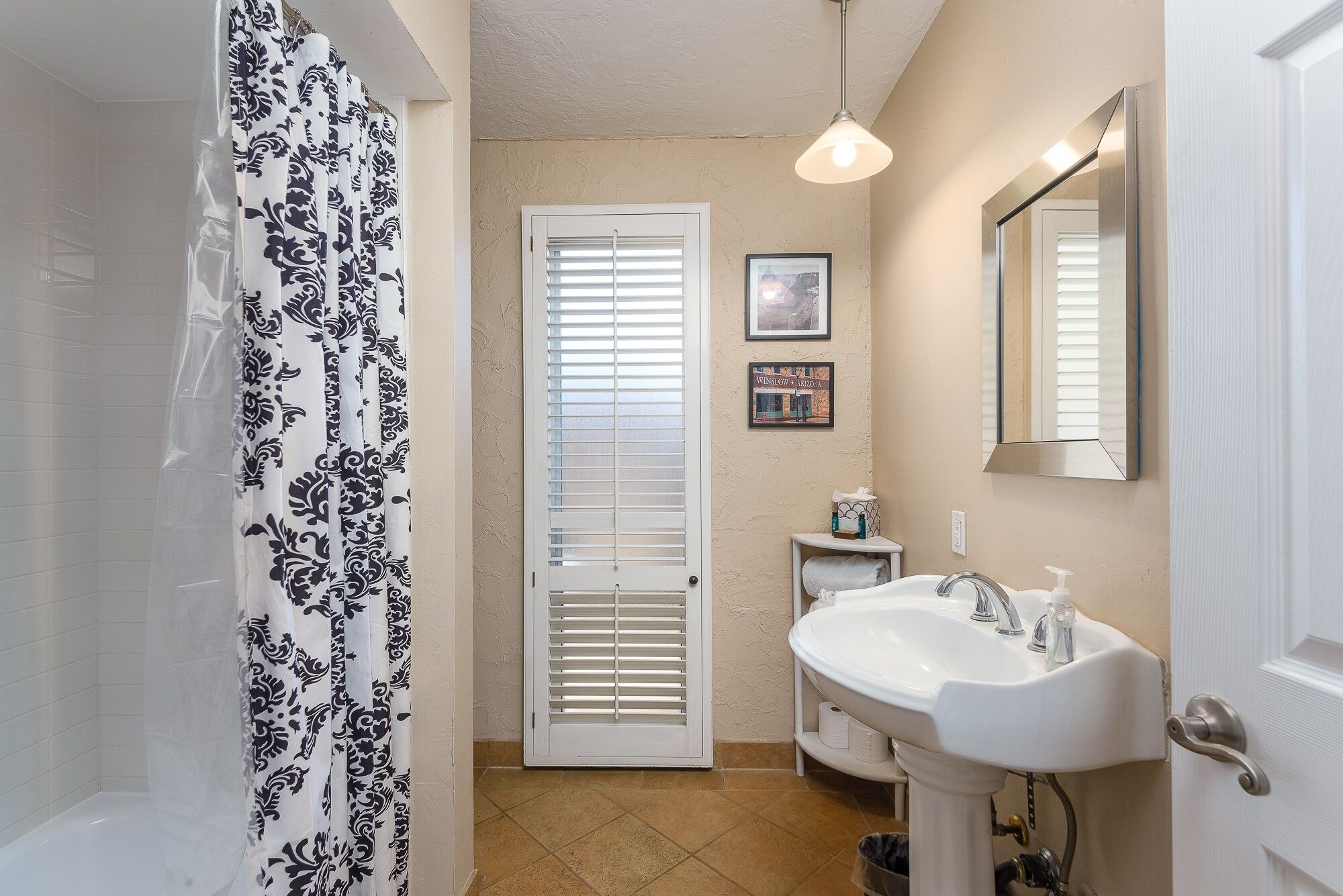 A bathroom with a shower curtain, a sink, a mirror, and a door with blinds.