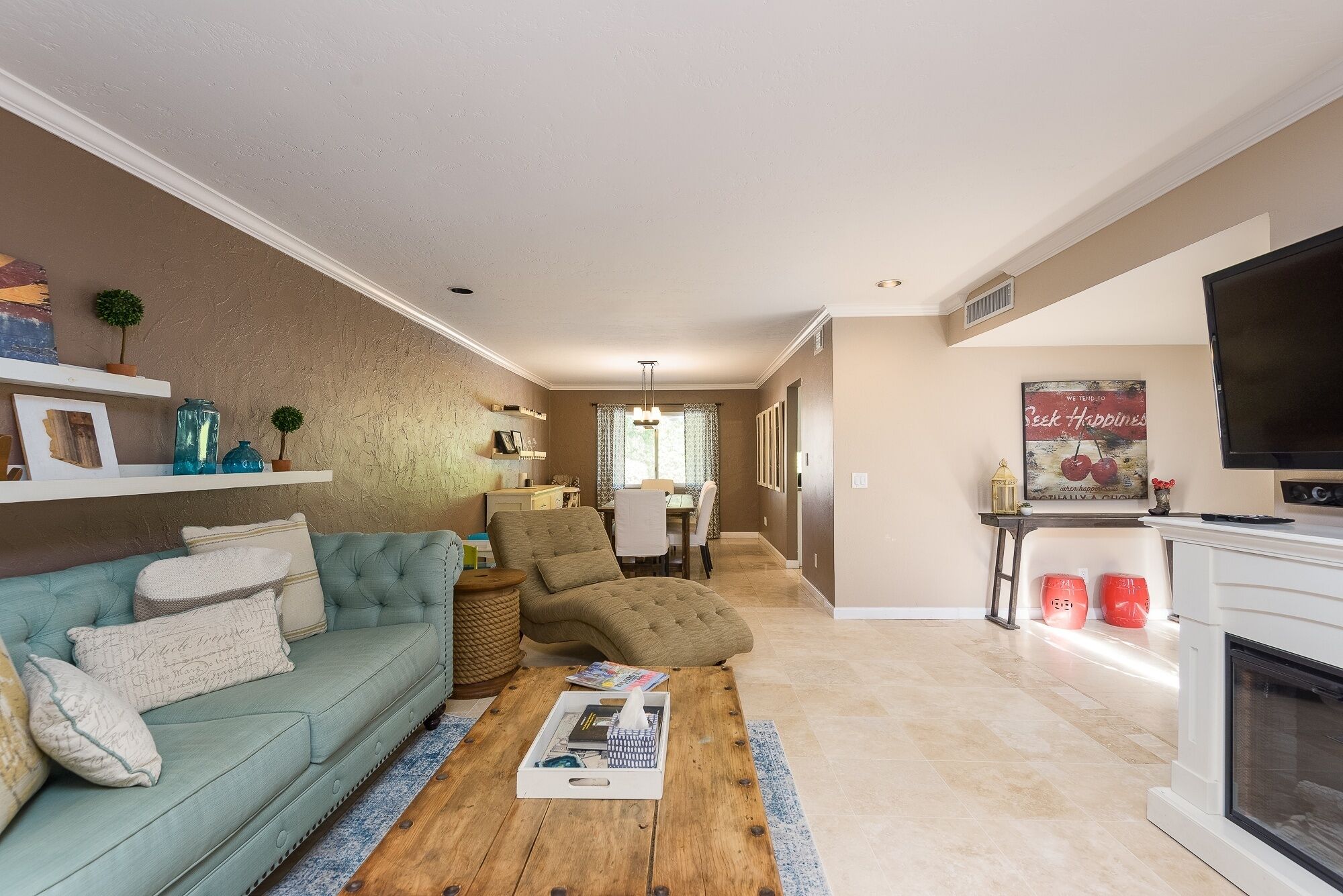 A living room with a sofa, coffee table, and TV. There is a dining area in the background.