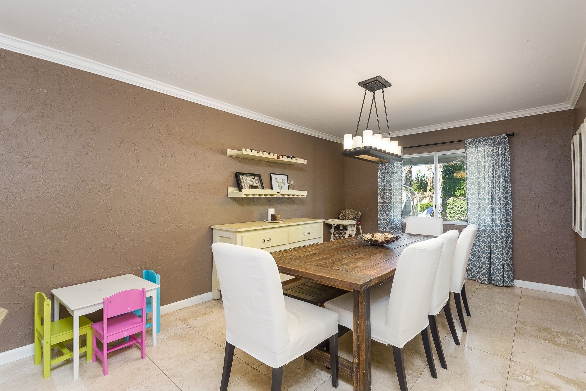 A dining area with a wooden table, white chairs, a small white table, and a children's table with colorful chairs.