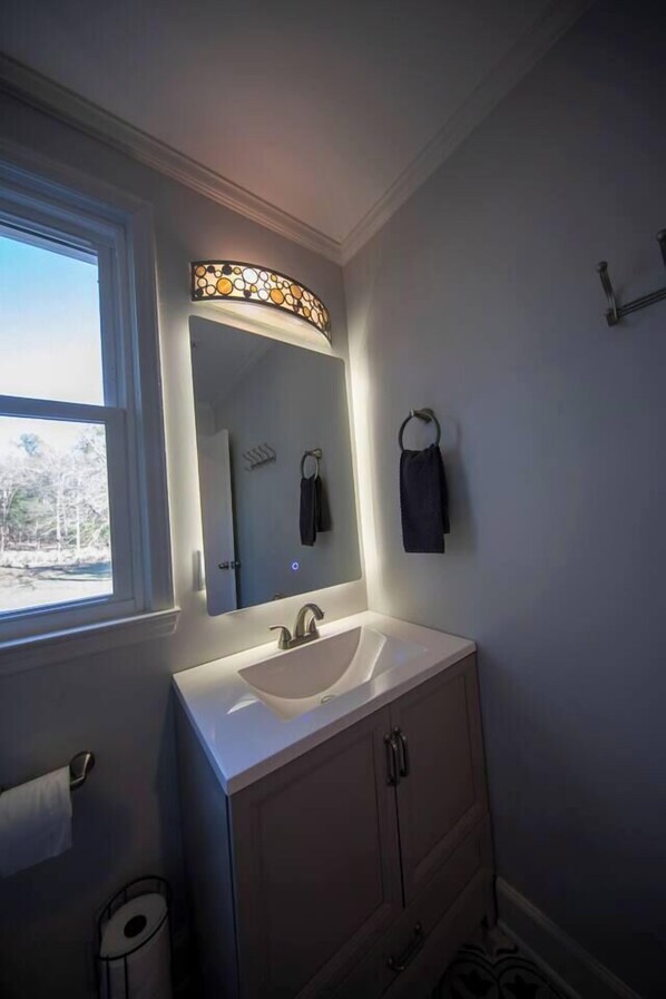 A bathroom with a white sink, a mirror with a stained glass light, a towel rack, and a window.