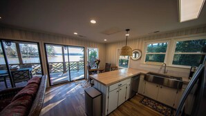 A modern kitchen with a large island, a dining area with a sofa, and a view of a lake through large sliding doors. - Sunsets and Ramp and Dock Access on Lake Wateree (Camden)