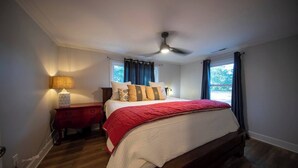 A bedroom with a bed, a nightstand, a lamp, a ceiling fan, and windows with curtains. - Sunsets and Ramp and Dock Access on Lake Wateree (Camden)