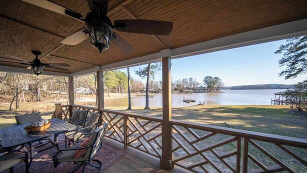 A covered outdoor deck with a table and chairs, overlooking a lake with a dock and trees. - Sunsets and Ramp and Dock Access on Lake Wateree (Camden)