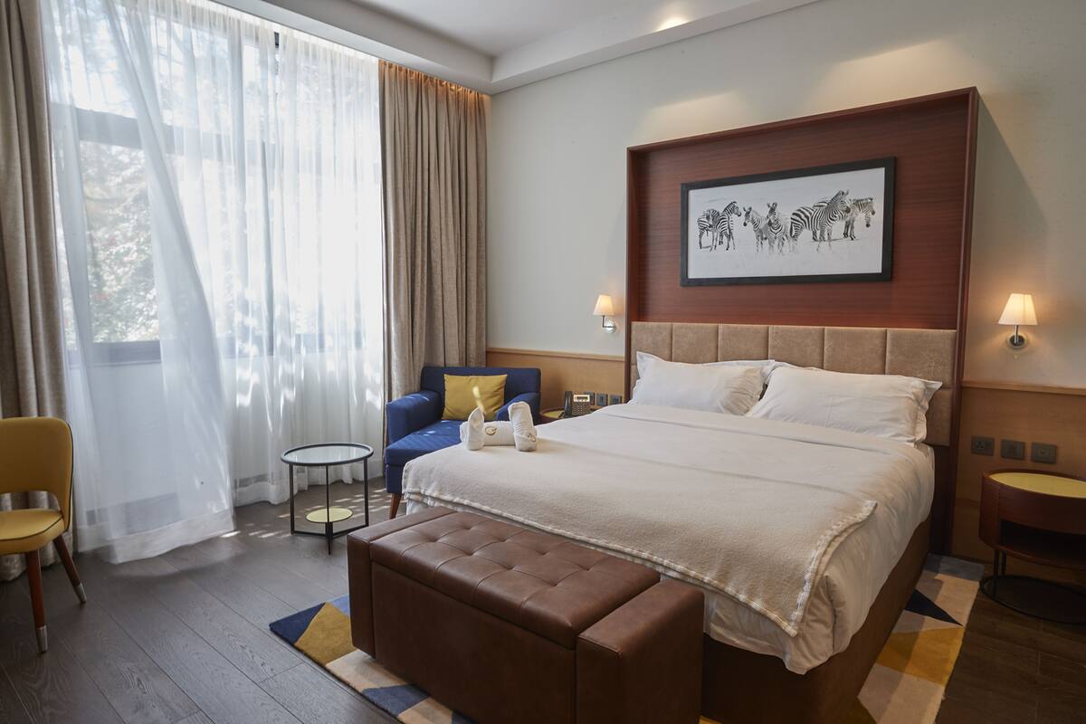 A hotel room with a large bed, a sofa, a small table, and a bench.