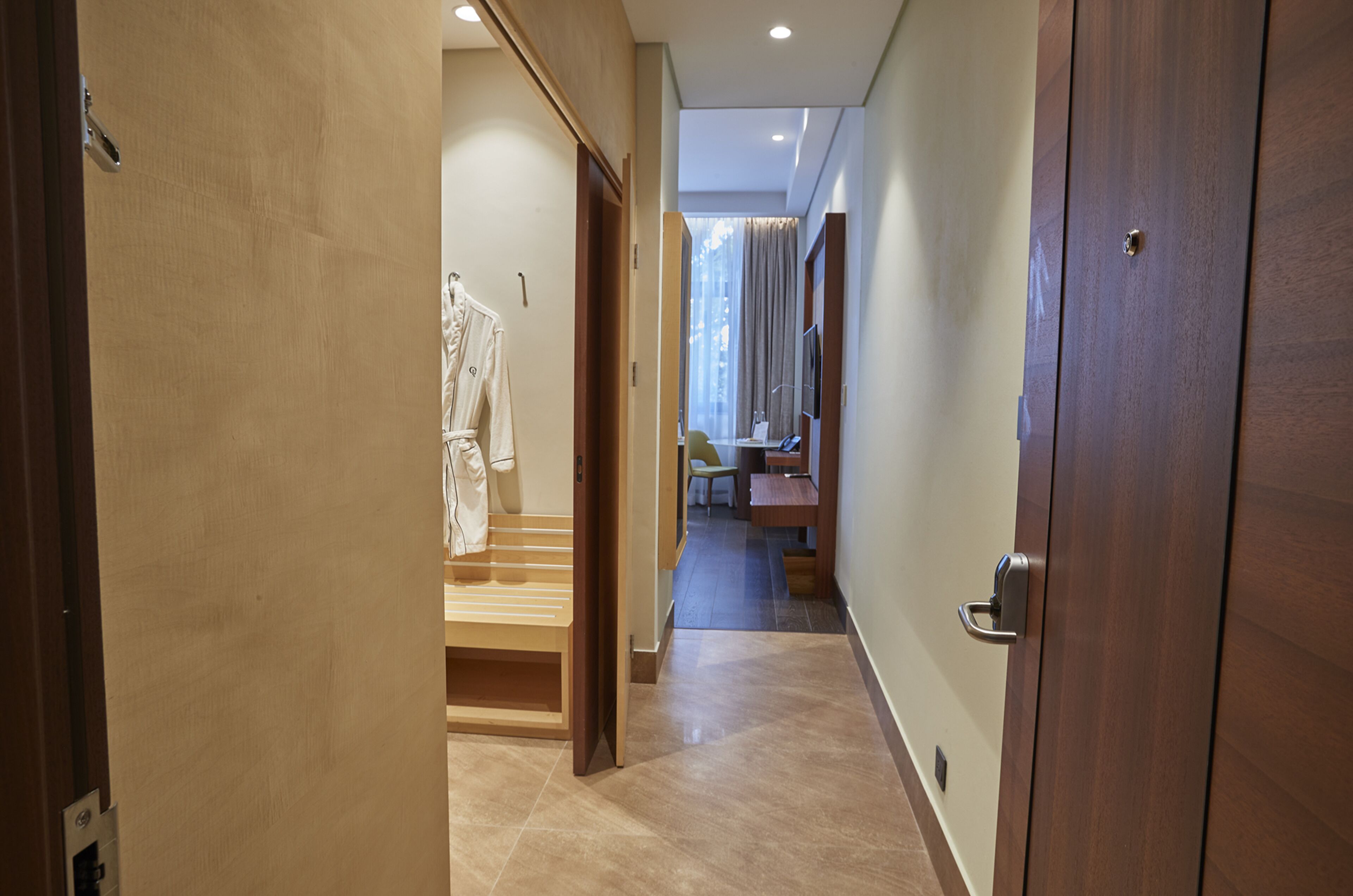 A hotel hallway with a wooden door, a bench, and a robe rack.