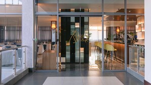 A modern hotel lobby with a glass entrance, a reception desk, and a bar area with bar stools. - The Quorum (Lusaka)