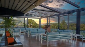 A modern outdoor lounge area with seating and planters, large windows offering scenic views. - The Quorum (Lusaka)