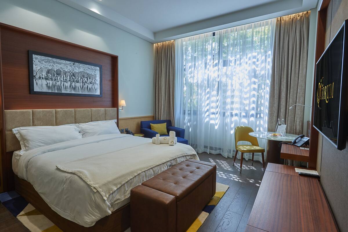 A hotel room with a large bed, a desk with a chair, a television, and a window with curtains.