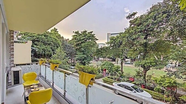 A balcony with yellow chairs and a table, overlooking a street with cars and greenery.