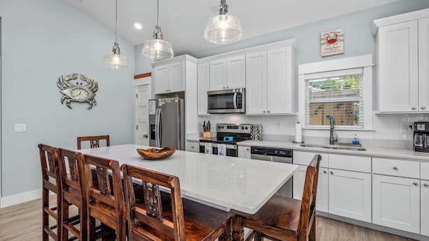 A modern kitchen with white cabinets, a central island, wooden chairs, and pendant lights.