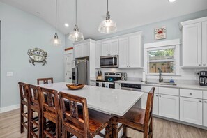 A modern kitchen with white cabinets, a central island, wooden chairs, and pendant lights.
