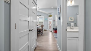 A hallway with white doors, a dining area with wooden chairs, and a bathroom with a sink and mirror.
