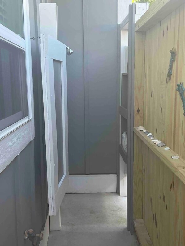 A narrow hallway with a grey door, a wooden shelf with decorative items, and a window with blinds.