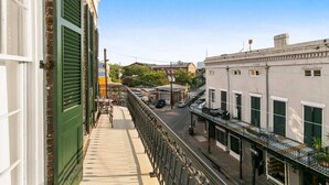 A balcony with a view of a street, a building with green shutters, and a clear sky.