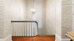Eine enge Treppe mit weißen Backsteinwänden, einem weißen Heizkörper und einer kristallenen Pendelleuchte.