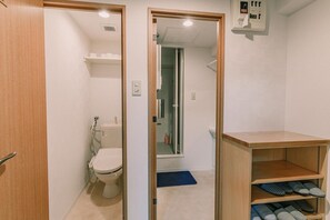 A compact bathroom with a toilet, a shelf with towels, and a small wooden cabinet.