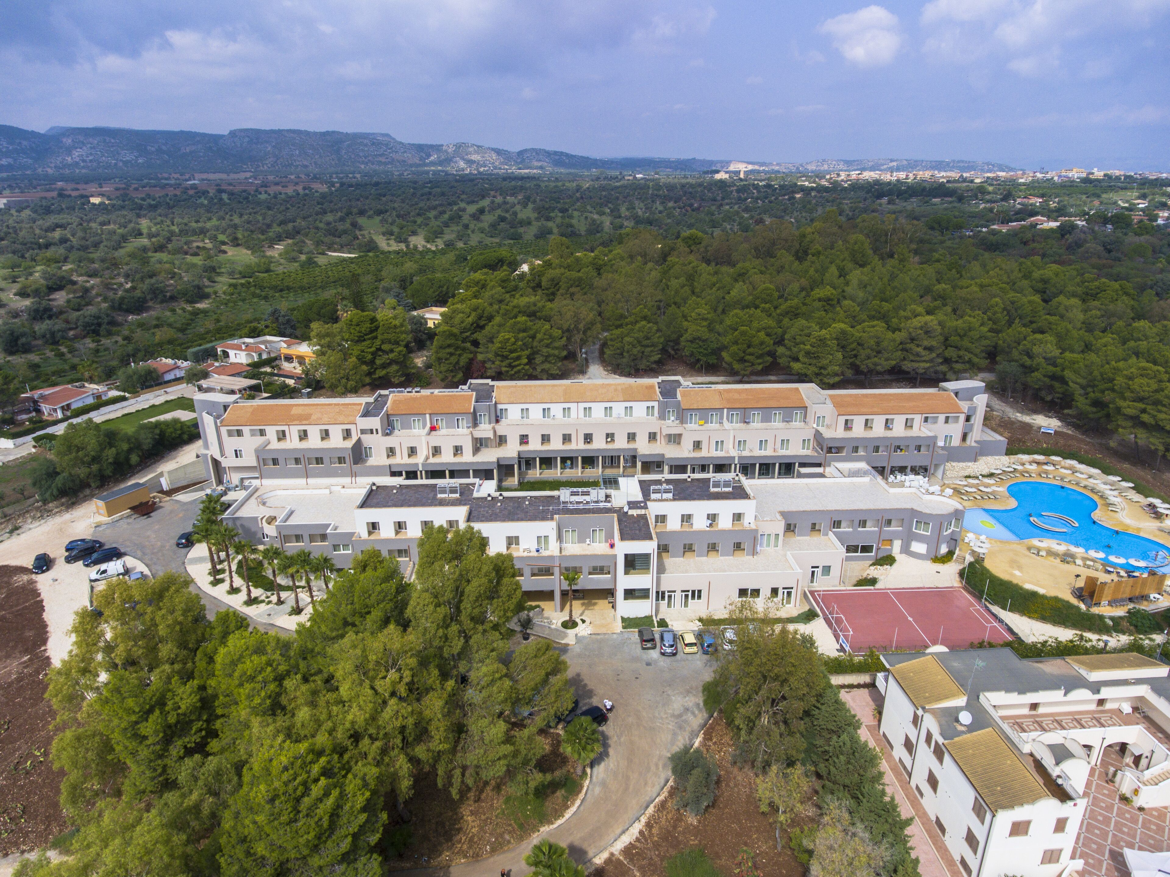 A large hotel with multiple buildings, a swimming pool, and surrounding greenery.