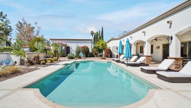 A pool area with lounge chairs and umbrellas, surrounded by a landscaped garden with cacti and trees. - Luxury 7BR Golf Mansion: Pool, Spa, Tennis Court (Scottsdale)