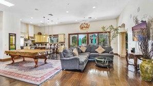 A spacious living room with a dining area, a gray sofa, and a coffee table. - Luxury 7BR Golf Mansion: Pool, Spa, Tennis Court (Scottsdale)
