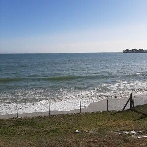 A coastal view with a fenced beach area, a grassy foreground, and a distant shoreline with trees. - Belle Villa Neuve Contemporaine, Directement sur mer Face à la Plage D'ezer (Loctudy)