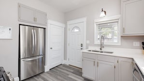A modern kitchen with white cabinetry, a stainless steel refrigerator, and a window above the sink.