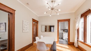 A spacious dining area with a white table and chairs, wooden flooring, and a modern chandelier.