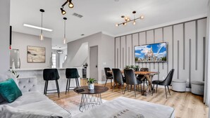 Una sala de estar moderna con un sofá gris, sillas negras, una mesa de comedor y un televisor montado en la pared.