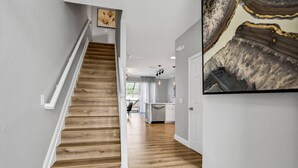 Una escalera con escalones de madera y barandillas blancas que lleva a una zona de cocina con armarios blancos y un ventanal.