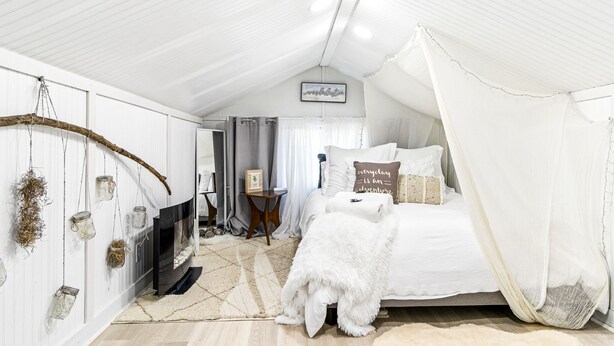 A cozy bedroom with a bed, a white dog, a fireplace, and a hanging branch.