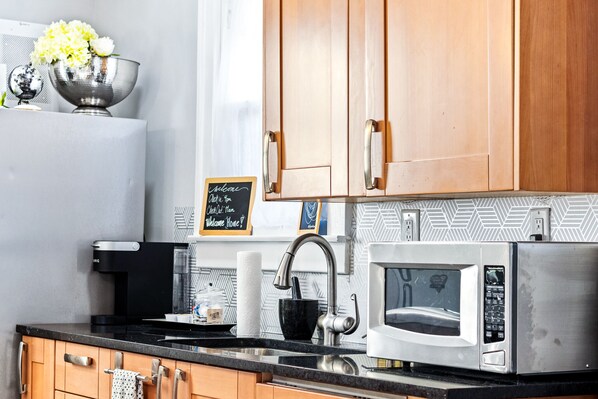 A modern kitchen with wooden cabinets, a stainless steel microwave, a black countertop, and a chalkboard sign.