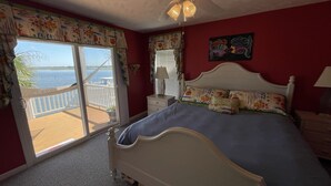 Un dormitorio con cama, ventilador de techo, ventana con vista al agua y balcón.