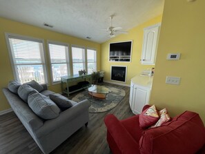 A living room with a gray sofa, a red chair, a glass coffee table, and a fireplace.