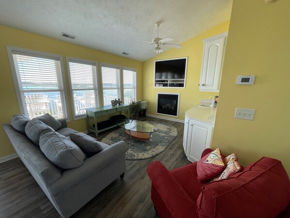 A living room with a gray sofa, a red chair, a glass coffee table, and a fireplace.