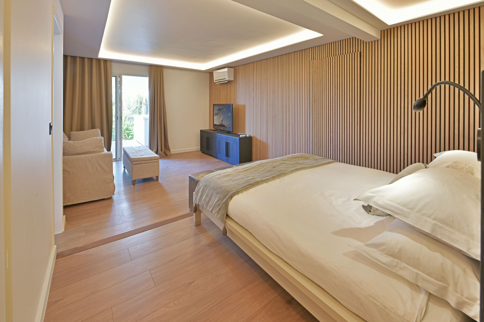 A modern hotel room with a large bed, a sofa, a small table, and a TV.