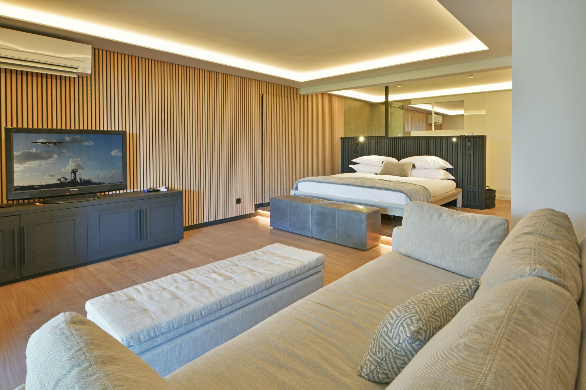 Una habitación de hotel moderna con una gran televisión de pantalla plana, una cama con cabecera, un sofá y un panel de pared de madera.