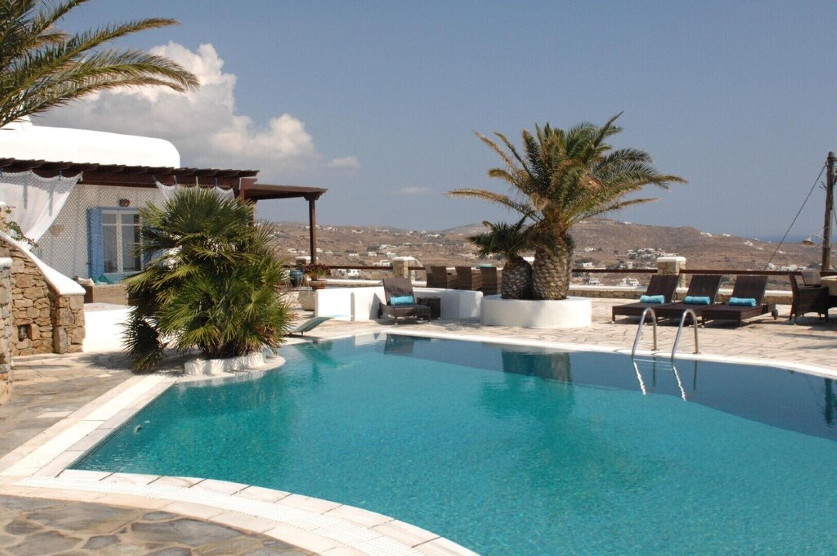 A pool with lounge chairs and palm trees, set against a backdrop of a mountainous landscape.