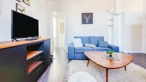 Una sala de estar moderna con un televisor de pantalla plana, un sofá azul, una mesa de centro de madera y un adorno en la pared.