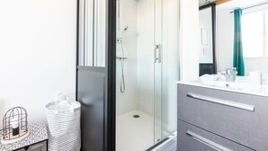 Un baño moderno con ducha acristalada, lavabo con espejo y una pequeña mesa con un objeto decorativo.
