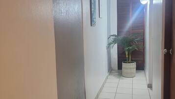 A hallway with white tiled flooring, a potted plant, and a door with a light fixture.
