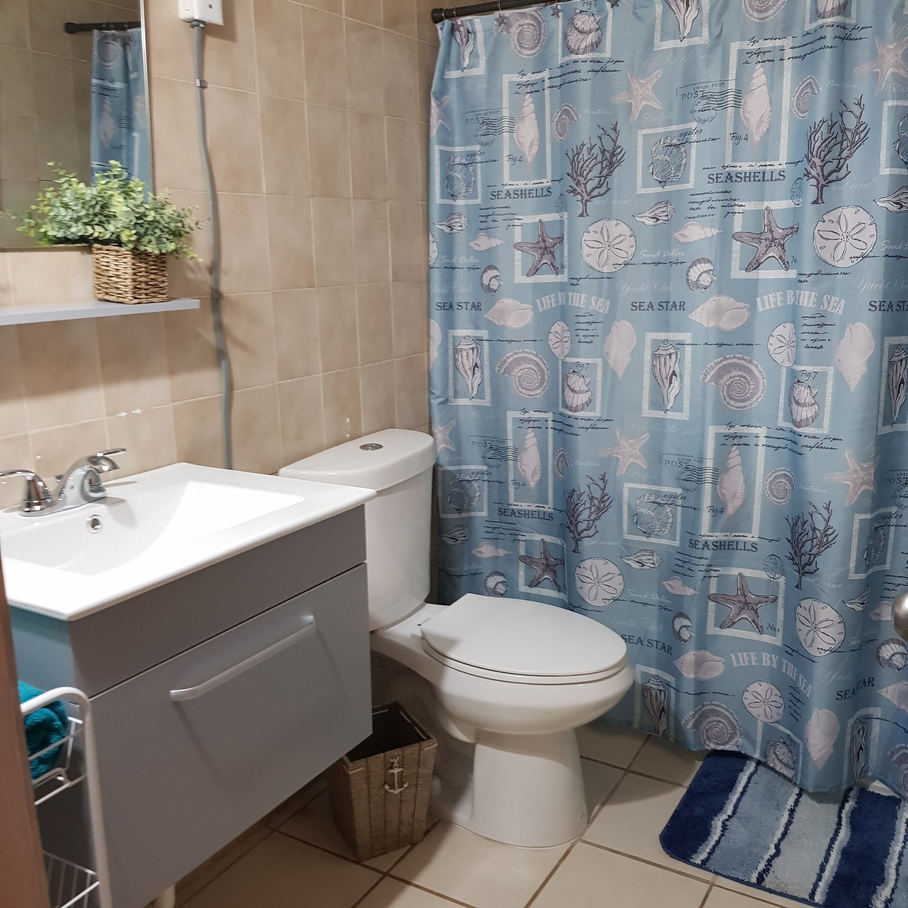 Un bany amb un lavabo blanc, vàter i cortina de bany blava amb dibuixos.